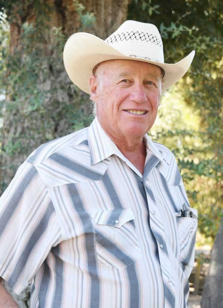 Senior man wearing cowboy hat smiling outdoors during Chamber of Commerce event.
