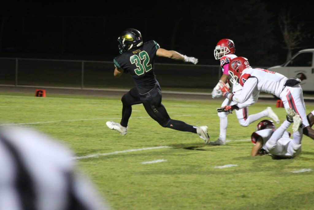 Football player in black jersey sprinting past defenders on the field.