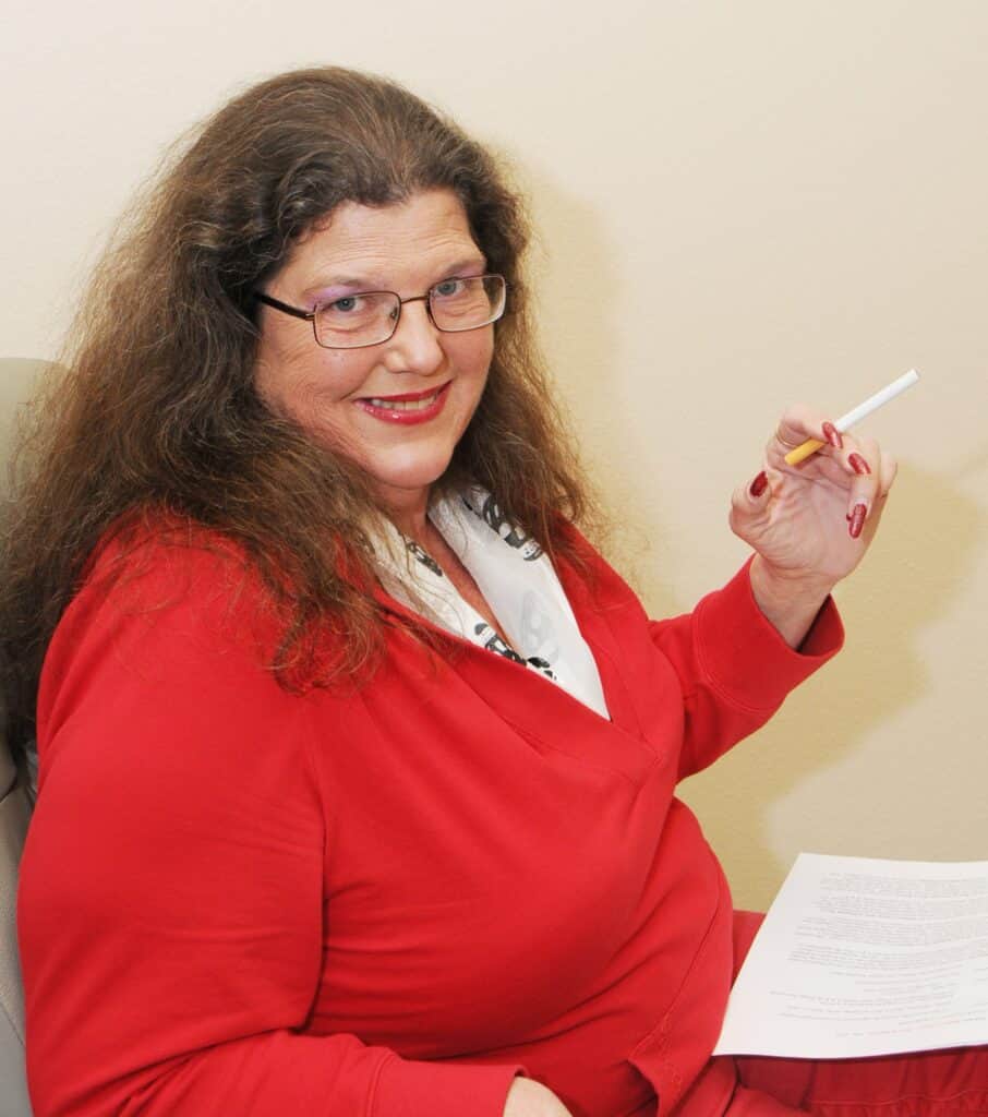 Portrait of Tami Jo Nix smiling, holding a pen and paper, celebrating her life and adventures.
