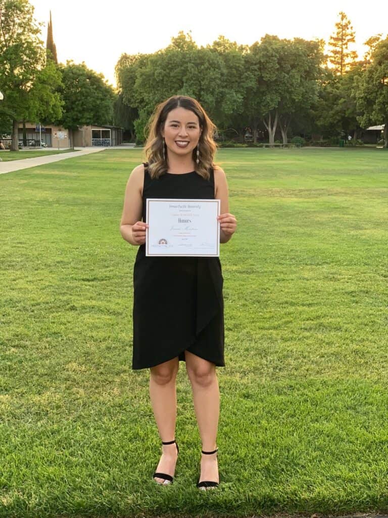 Young woman holding certificate outdoors during award ceremony in Fresno Pacific campus.
