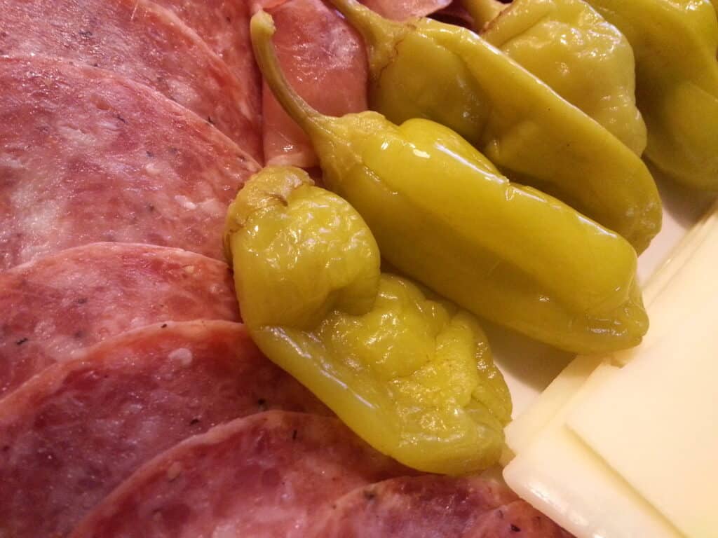 Sliced salami with green pepperoncini peppers on a serving platter.