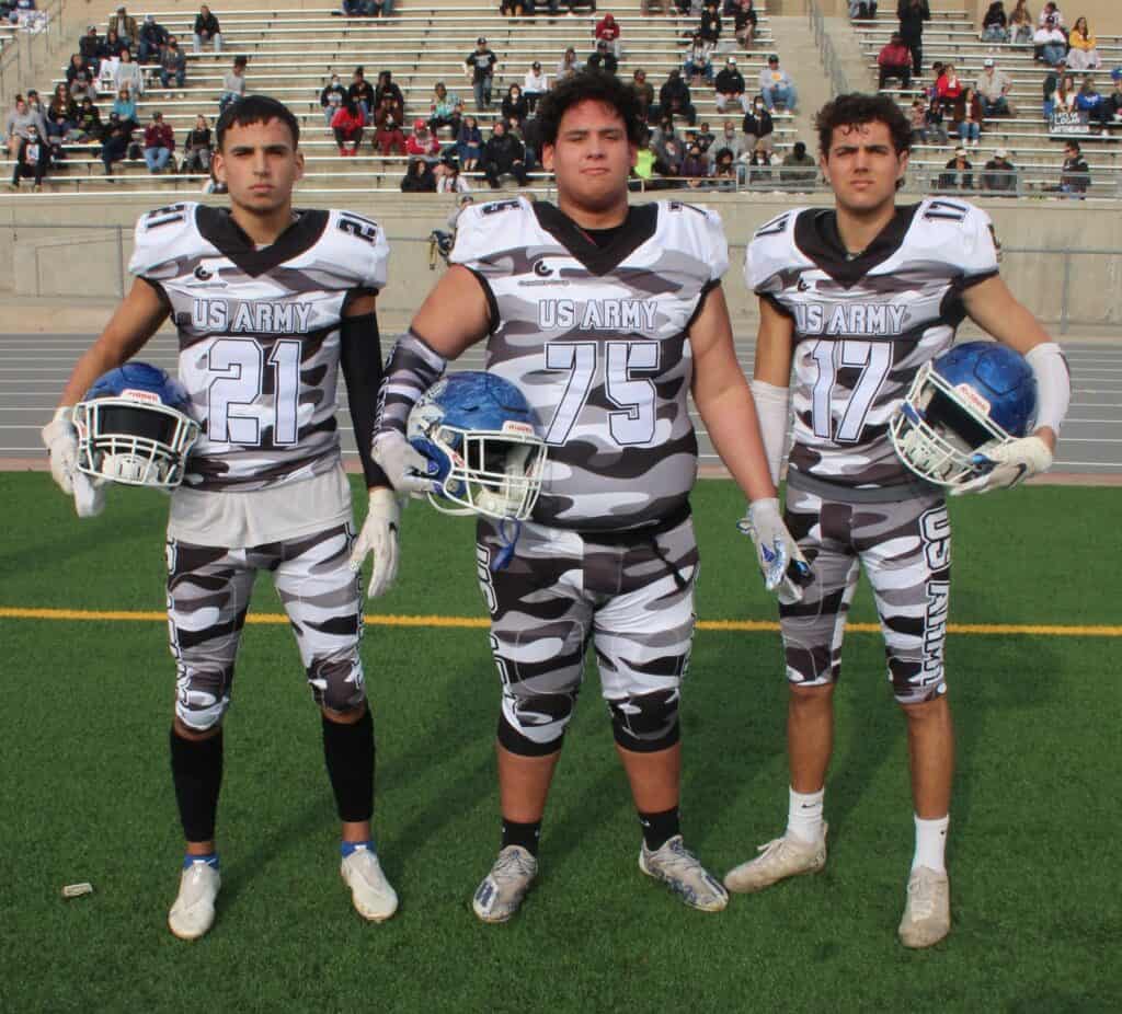 Three Madera Coyotes football players in US Army uniforms on field.