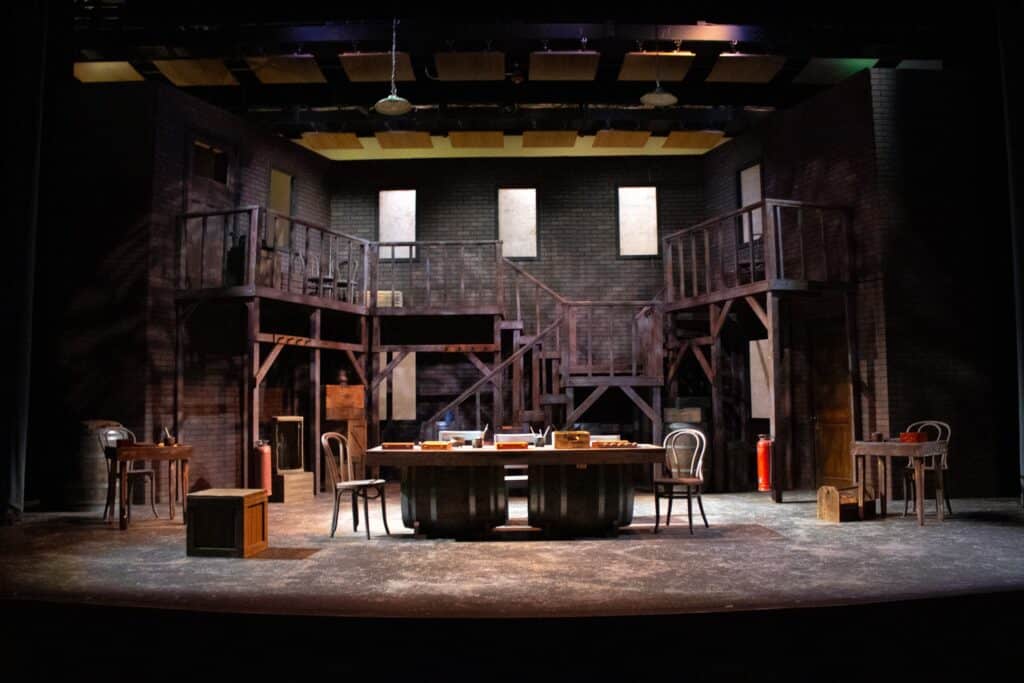 Stage set featuring a historic courtroom scene with wooden furniture and elevated platforms.