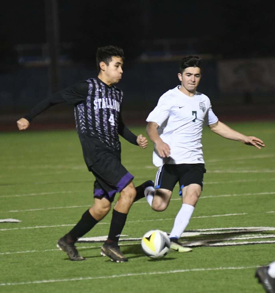 Two soccer players competing for the ball during a match at night.
