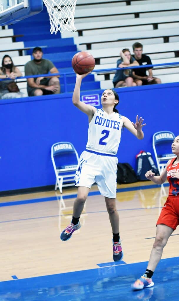 Young female basketball player in blue Coyotes uniform jumping for shot during game.