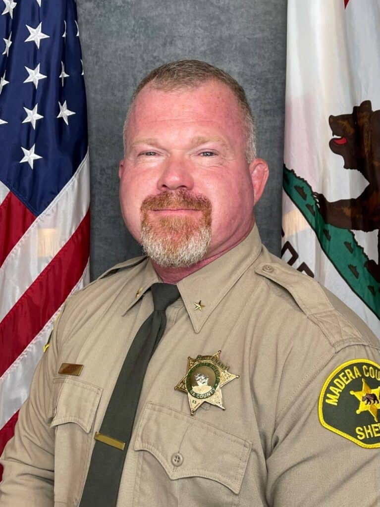 Madera County Sheriff with new Assistant Sheriff in front of flags.