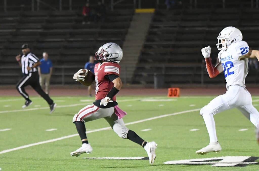 Madera High football player running with ball against Immanuel defenders.