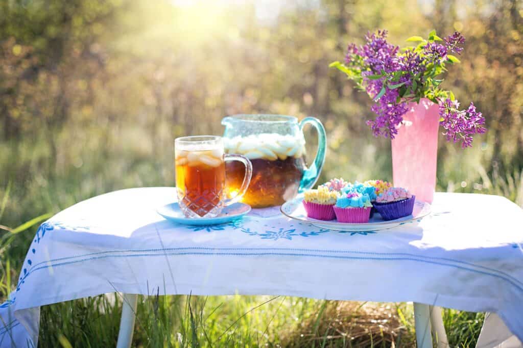 Relaxing outdoor scene with iced tea, beer, cupcakes, and flowers.