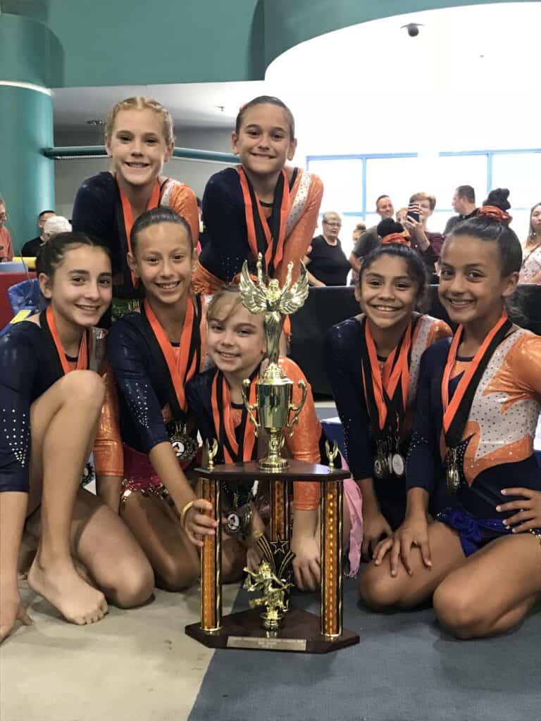 Group of young gymnasts celebrating their victory with a trophy at Clovis meet.