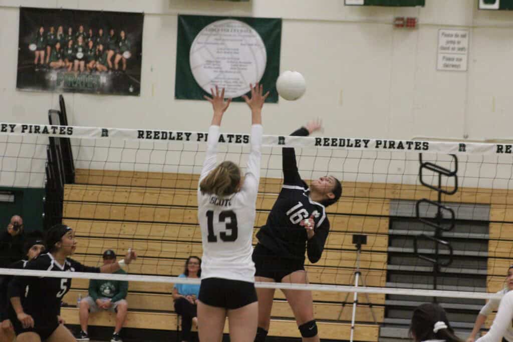 Madera volleyball player blocks the ball against Reedley Pirates in a tense match.