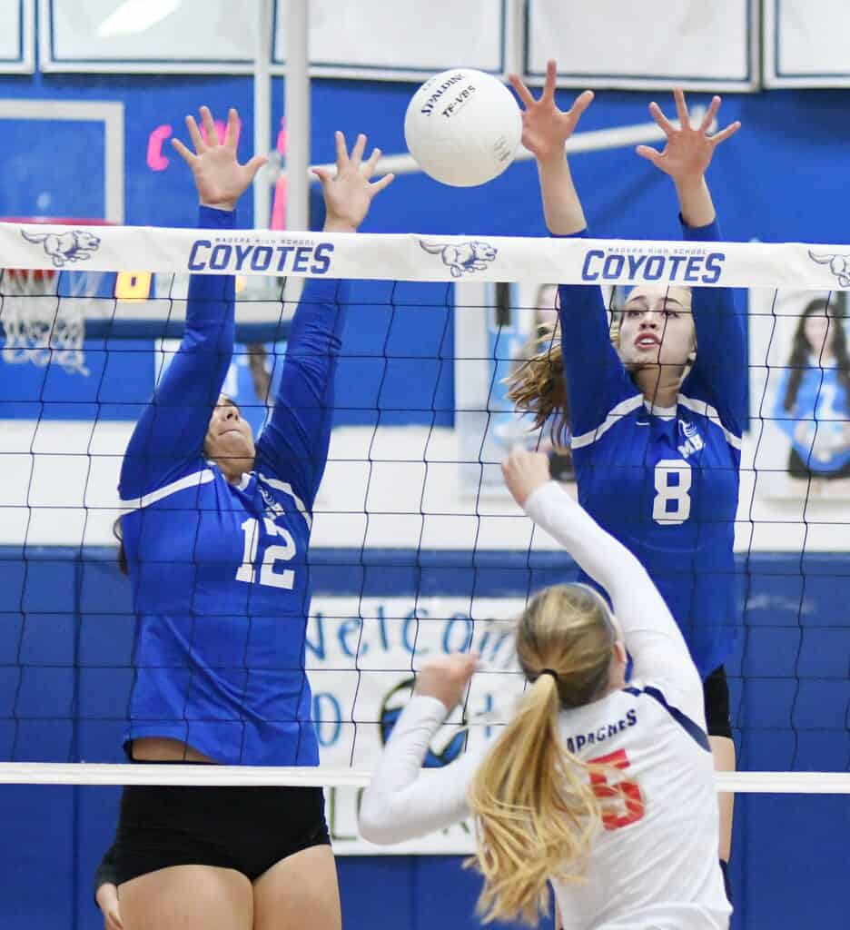 Coyotes volleyball players blocking at the net during a match.