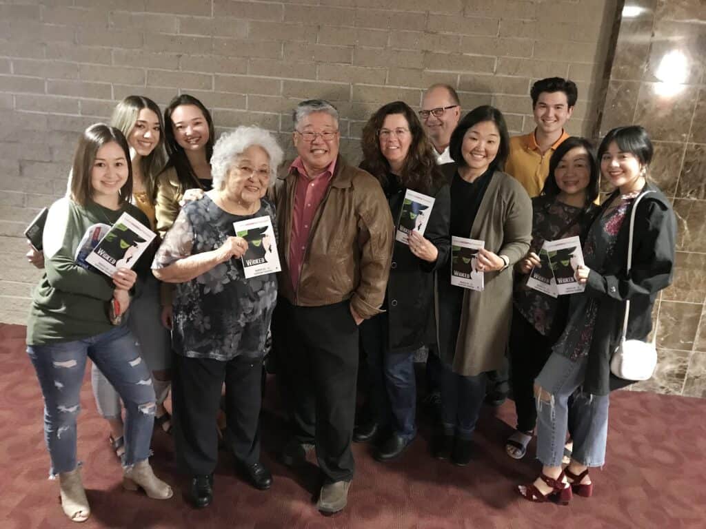 Group of diverse people holding programs at Saroyan theater during 'Wicked' lights event.