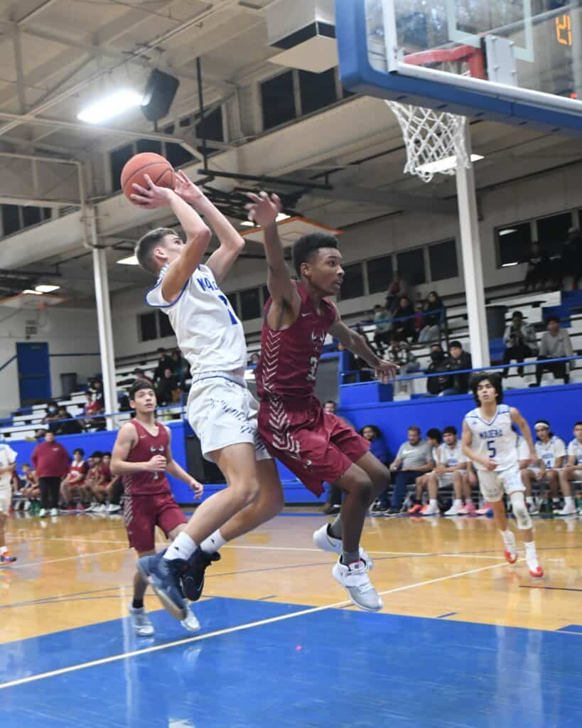 Young basketball player drives to the hoop against defender in gym.