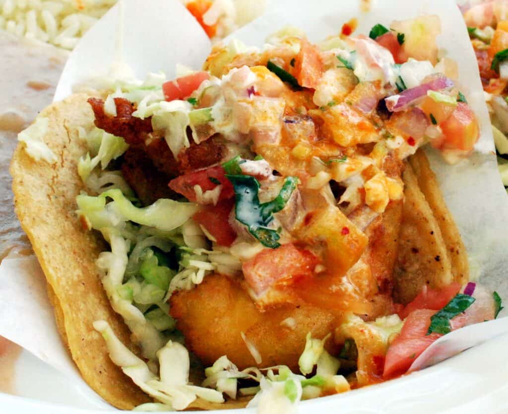 Delicious taco with fresh vegetables and crispy fries on a paper-lined plate.
