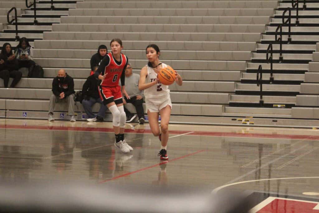 Female basketball player dribbling ball during game in Madera gymnasium.