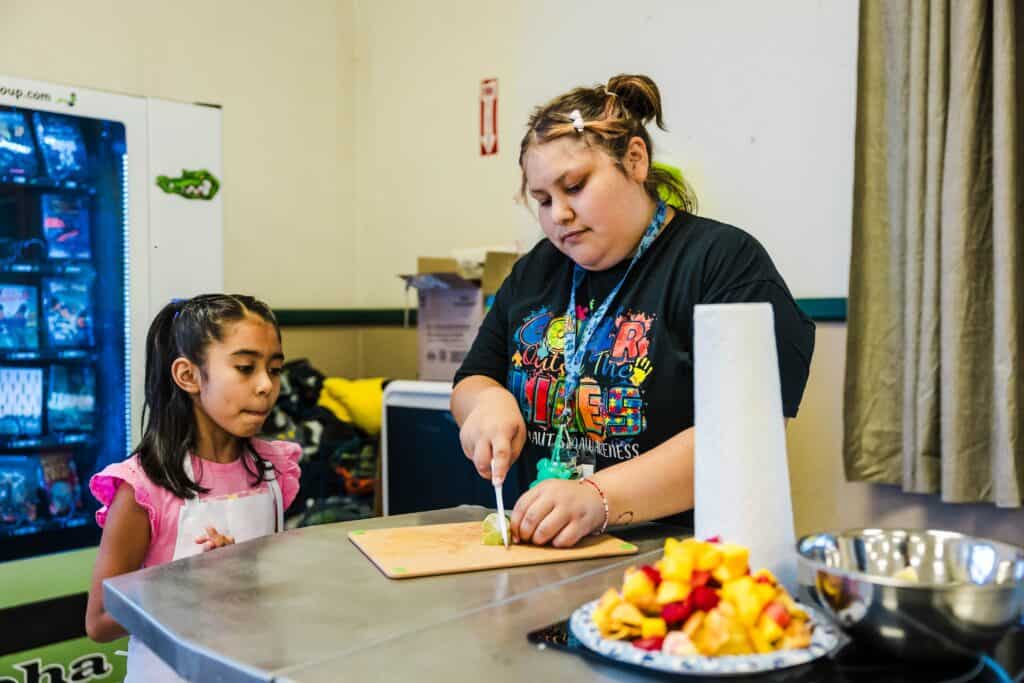 Young girl cooking with instructor at Madera Summer Squad Camp.
