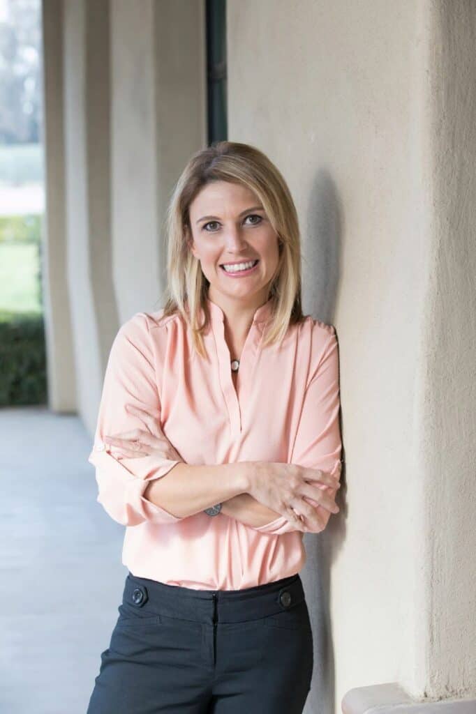 Woman smiling outdoors, standing against a wall, representing progress and success.