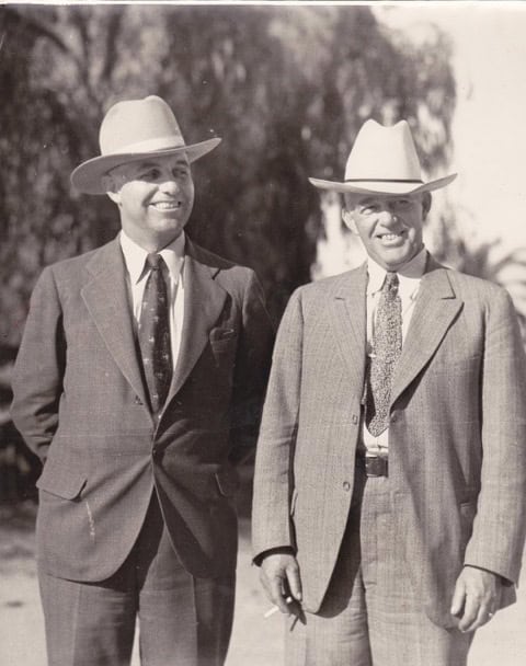 Two boys in suits and hats smiling outdoors, historical school scene.