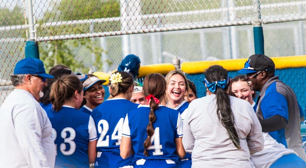 Madera Coyotes softball team celebrating coach’s 700th win after game victory.
