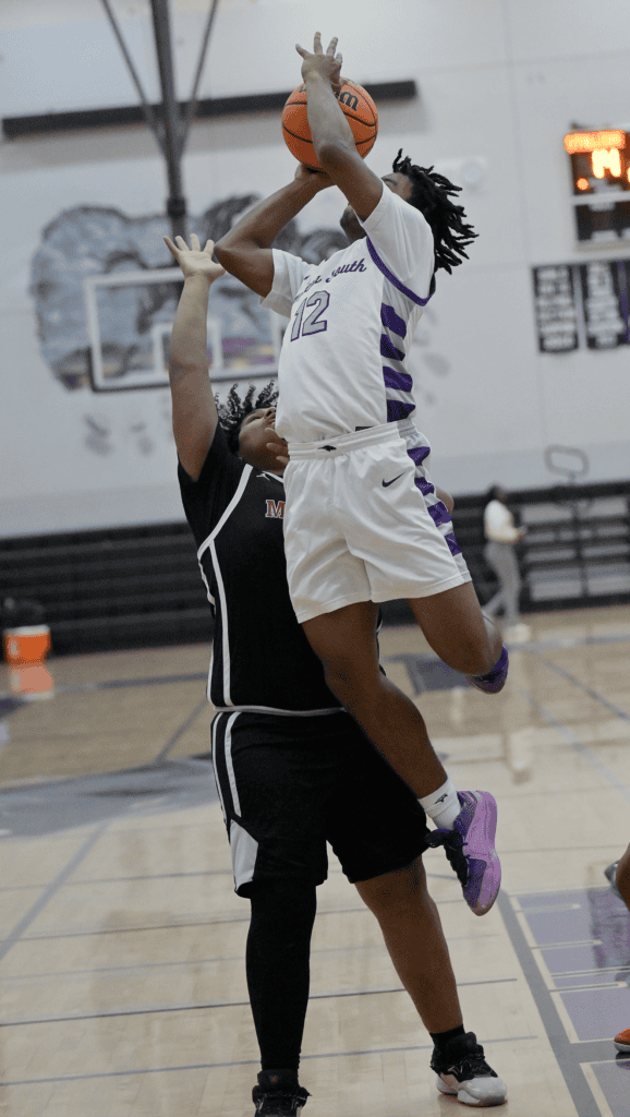 Player in white jersey jumps for shot over defender in black jersey during game.