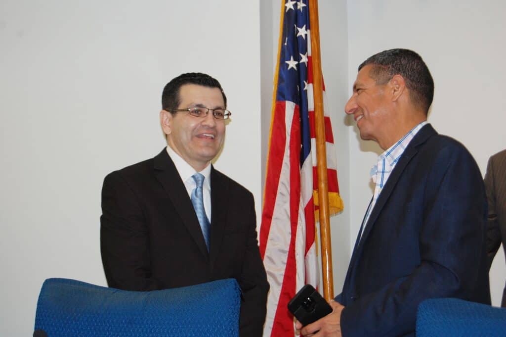 Two men in discussion with American flag in background.