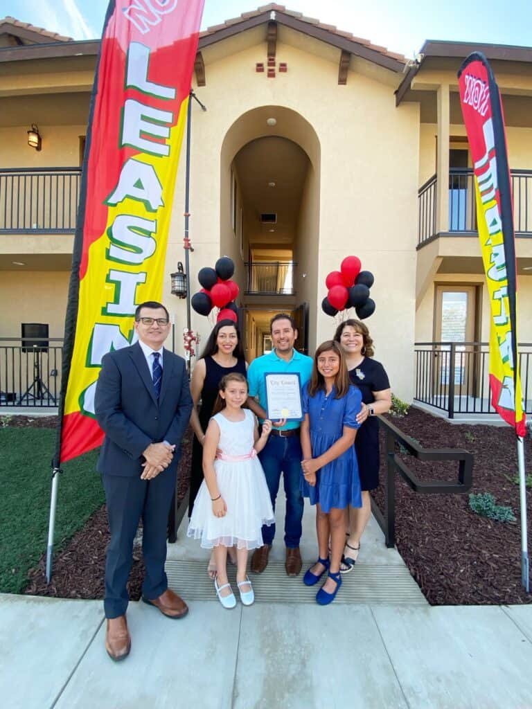 Group of graduates and family celebrating outside apartment building with balloons and banners.
