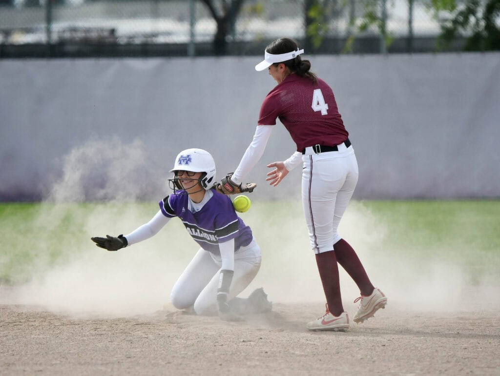 Female softball player in maroon uniform tags out opponent sliding into base.