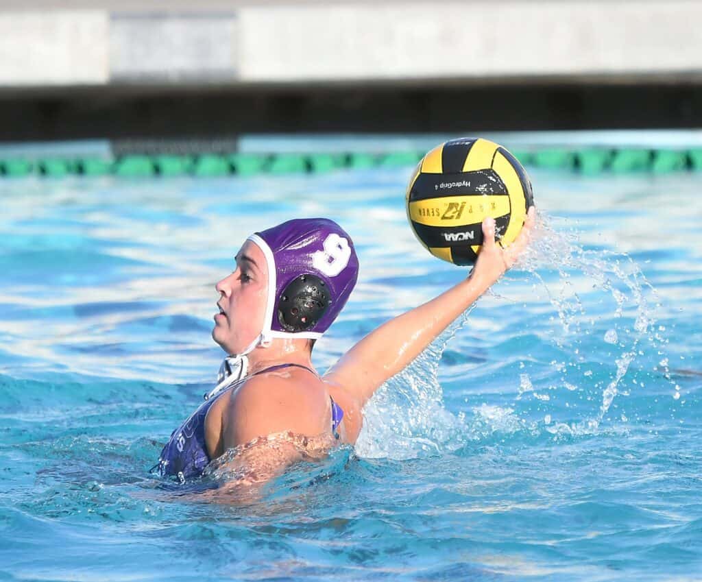 Rivera twins competing in water polo match, holding a ball in the pool.