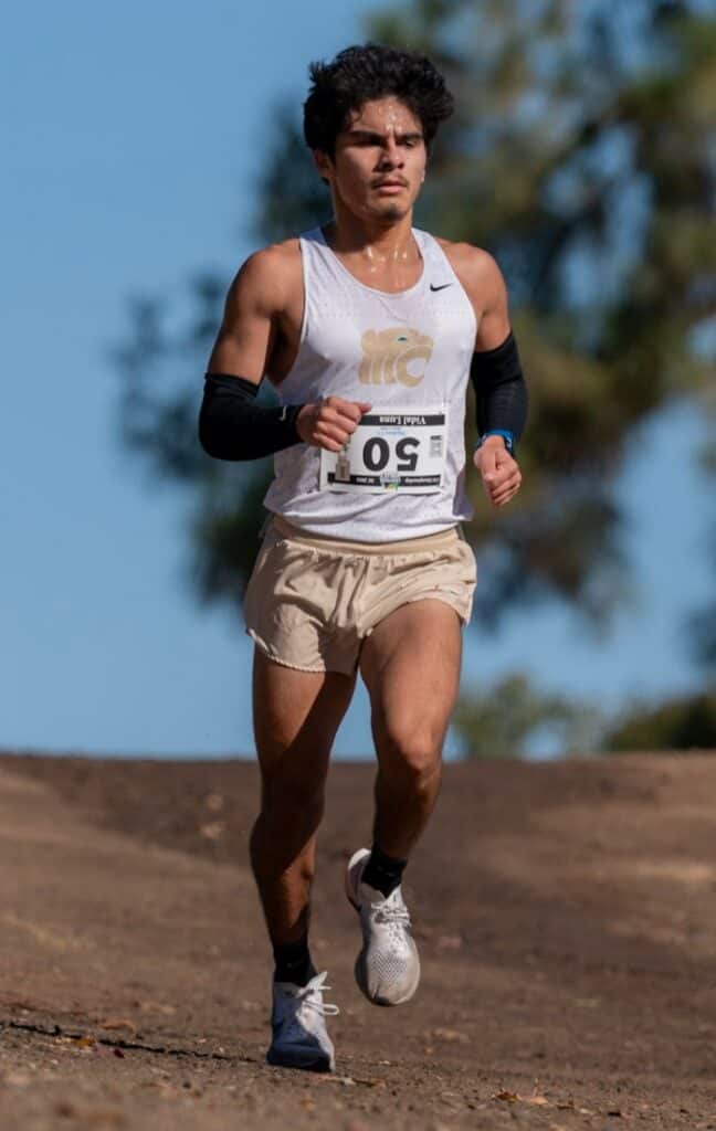 Young male cross country runner competing outdoors during daytime.