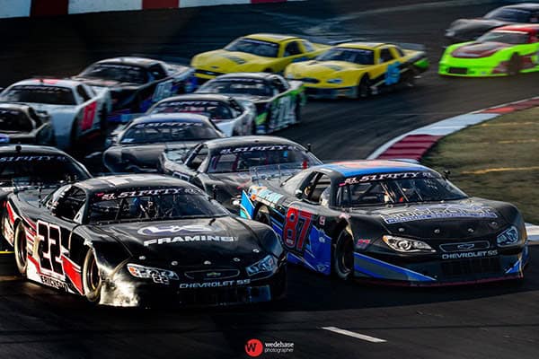 Action-packed speedway racing with multiple cars on track at Madera Speedway.