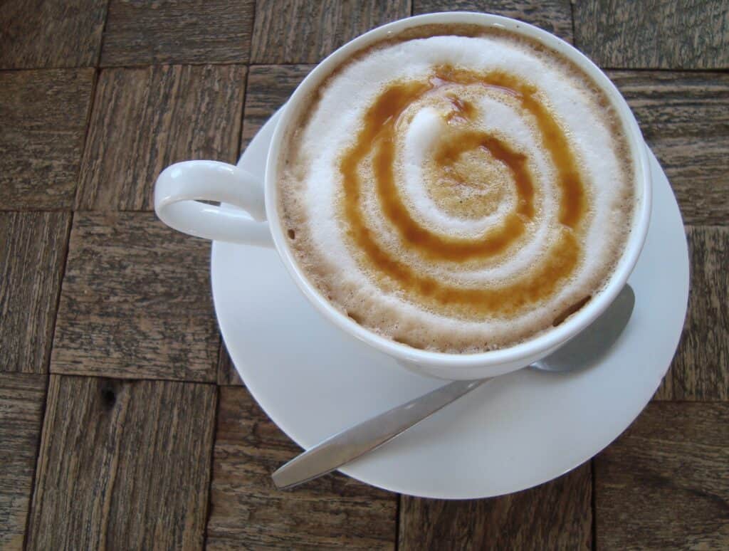 Whipped cream coffee with caramel drizzle on top, served in a white cup on a wooden table.